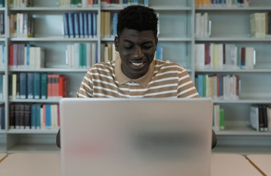 Young African student using laptop in library - School education concept
